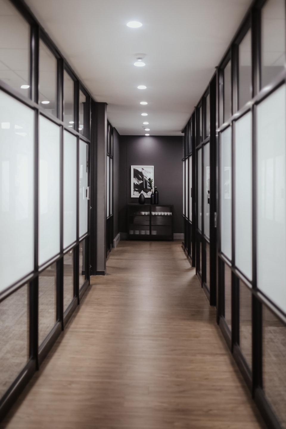 Modern office hallway with glass partitions and wooden flooring.