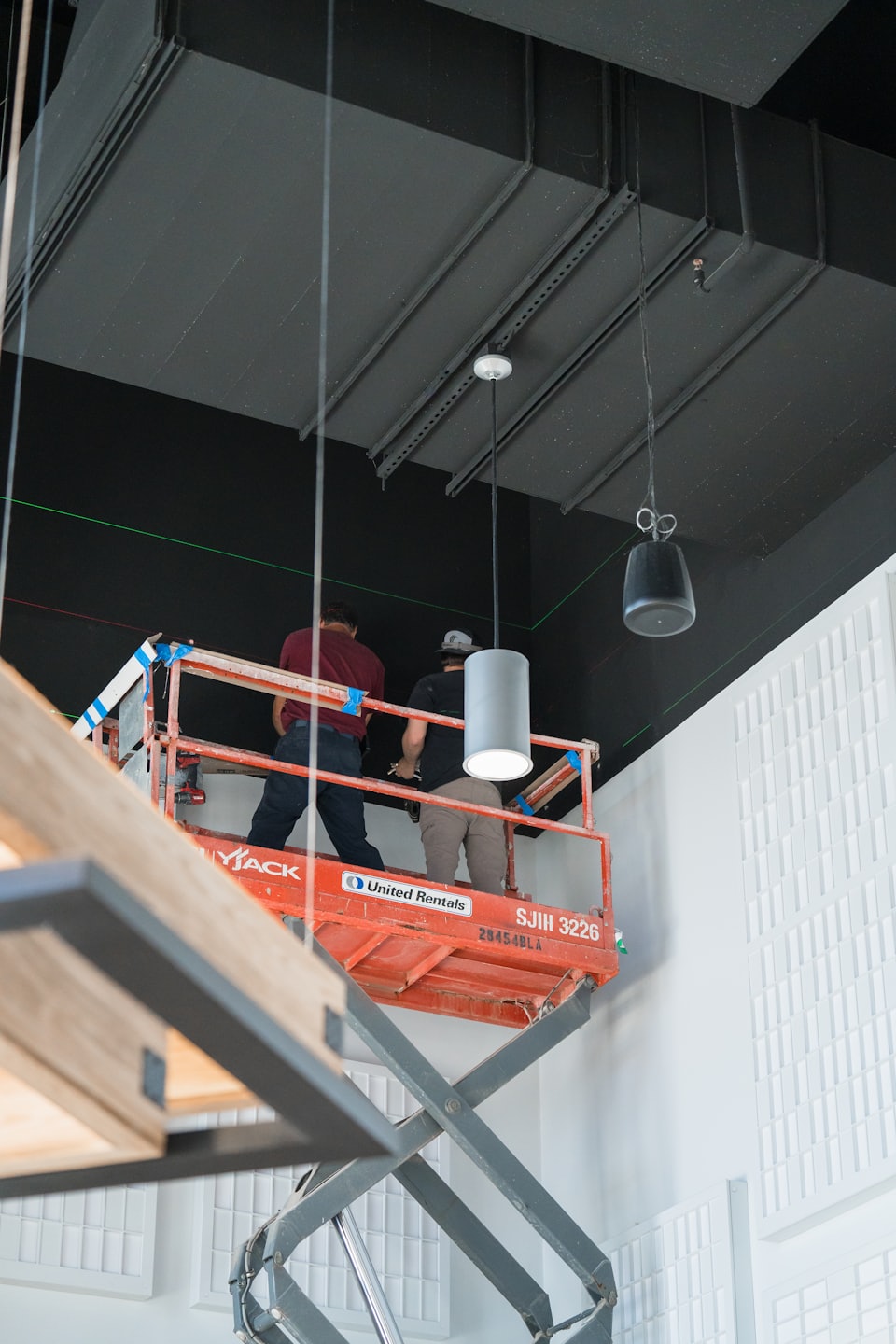 Men on scissor lift working on exposed ceiling in commercial building.