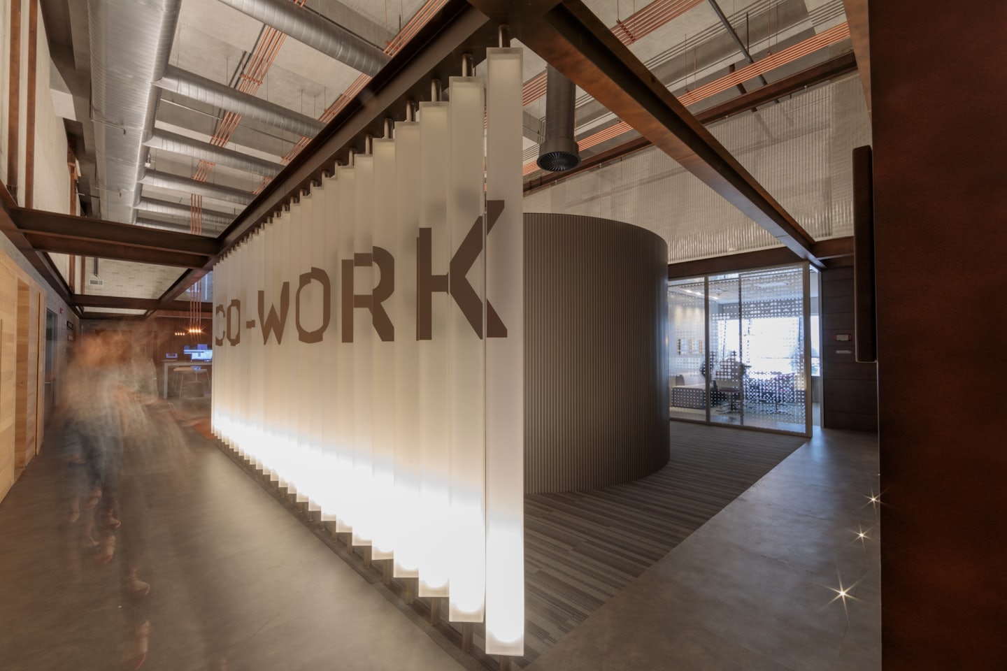 Coworking office space with translucent partition and exposed pipes.
