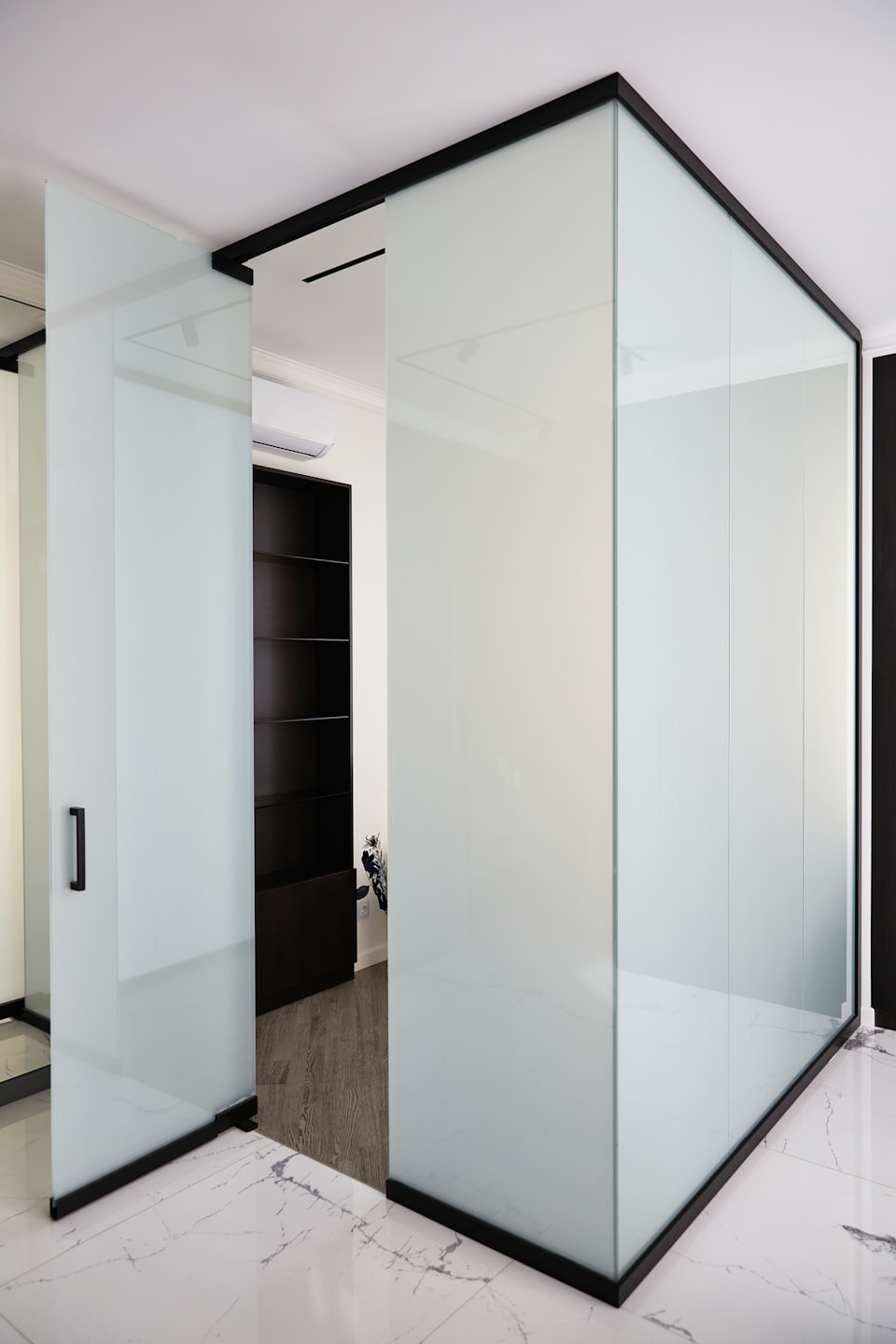 Frosted glass partitions with black frames divide a modern office.