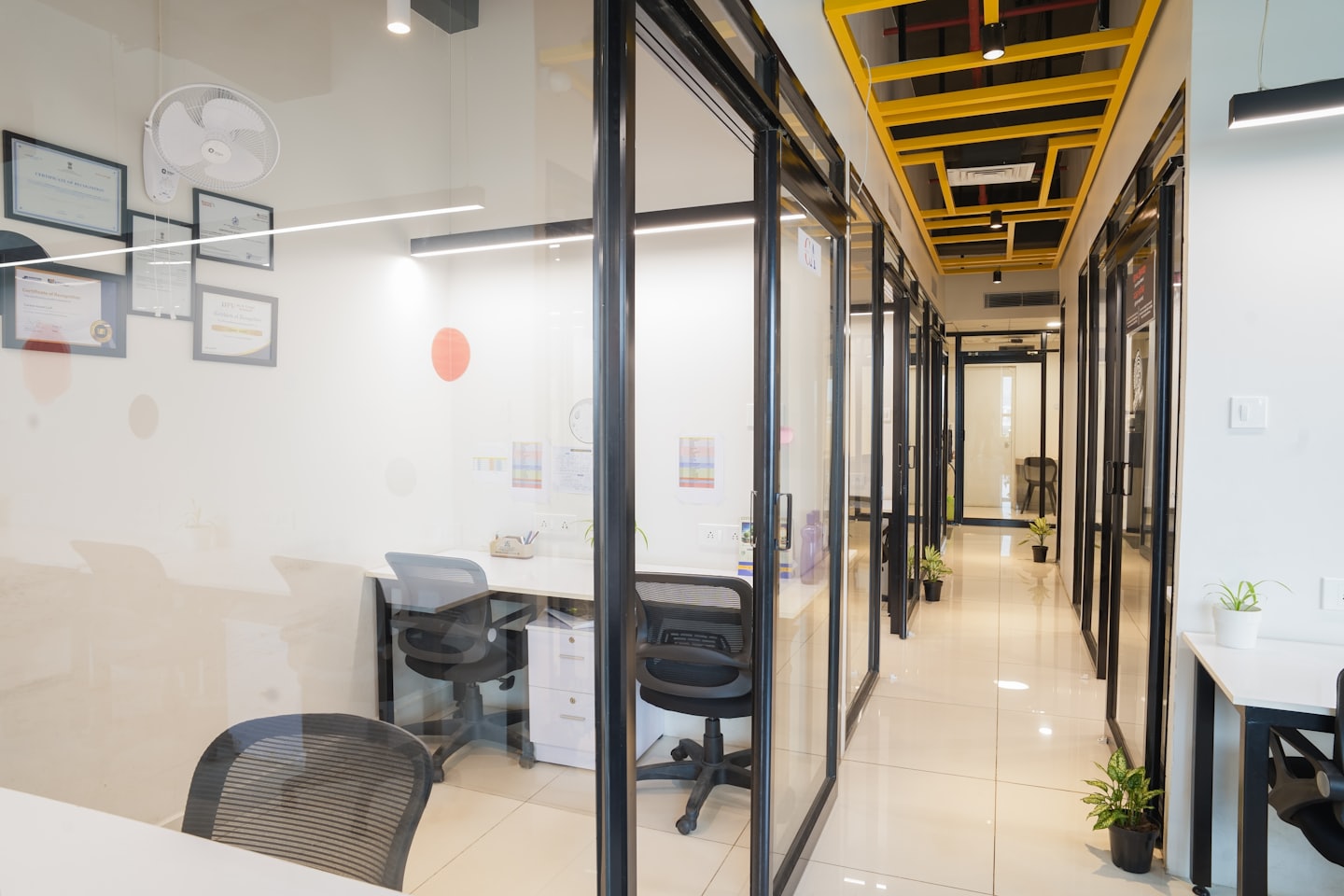 Modern office hallway featuring private workspaces and yellow grid ceilings.